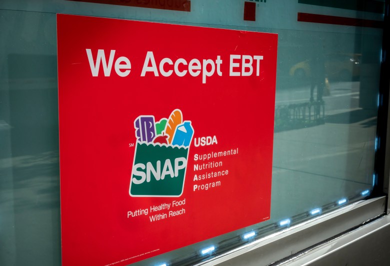 A red sign posted on a store window reads "We Accept EBT" and features the SNAP (Supplemental Nutrition Assistance Program) logo with the text "Putting Healthy Food Within Reach."