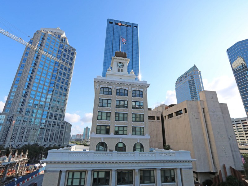View of downtown Tampa skyline centered on the historic City Hall building with its clock tower, flanked by much taller, modern glass skyscrapers, including the PNC Bank building.