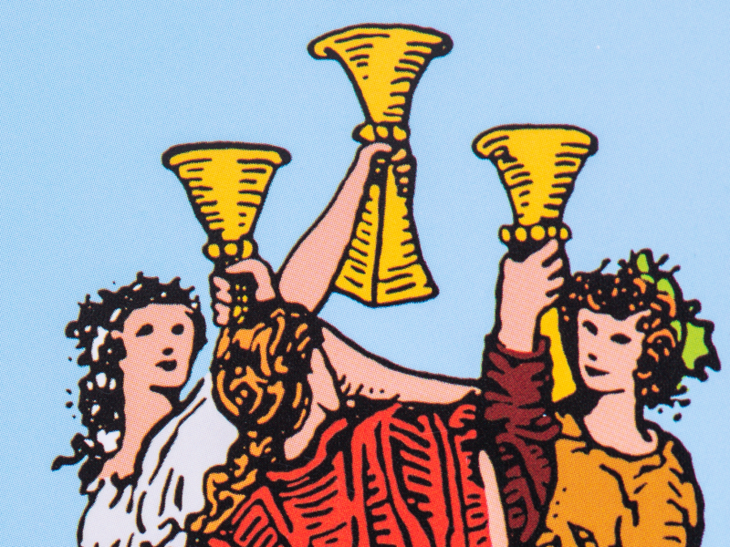 Close-up illustration of the Three of Cups Tarot card from the Rider-Waite deck, showing three figures celebrating together by raising three golden cups against a blue background.